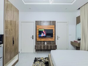 A modern bedroom with a TV mounted on a wooden panel, a bed, a bedside table with books, and a wardrobe. - Special Studio Apartment in Victoria Island with Pool, Fast Wi-Fi & 24/7 Power (Lagos)