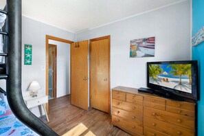 A room with a wooden dresser, a television displaying a beach scene, a door, and a wall with a framed picture. - Down by the Bay an Oceanside hot tub, and pet-friendly (Kill Devil Hills)