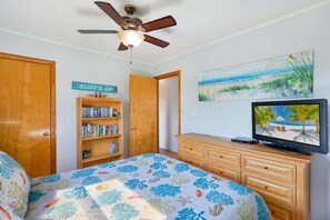A bedroom with a bed, a bookshelf, a television, and a ceiling fan. - Down by the Bay an Oceanside hot tub, and pet-friendly (Kill Devil Hills)