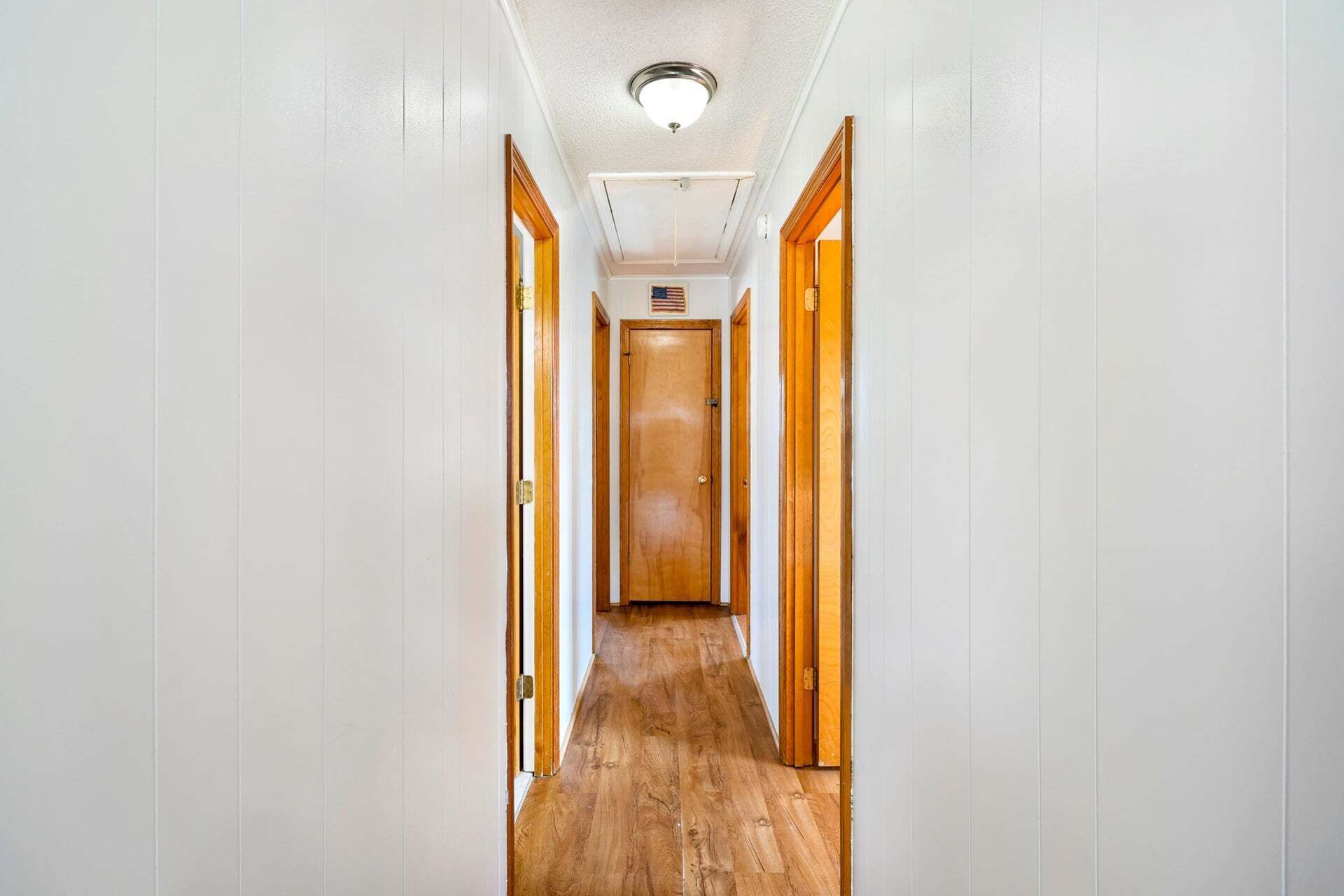 A narrow hallway with wooden doors on both sides and a wooden floor.