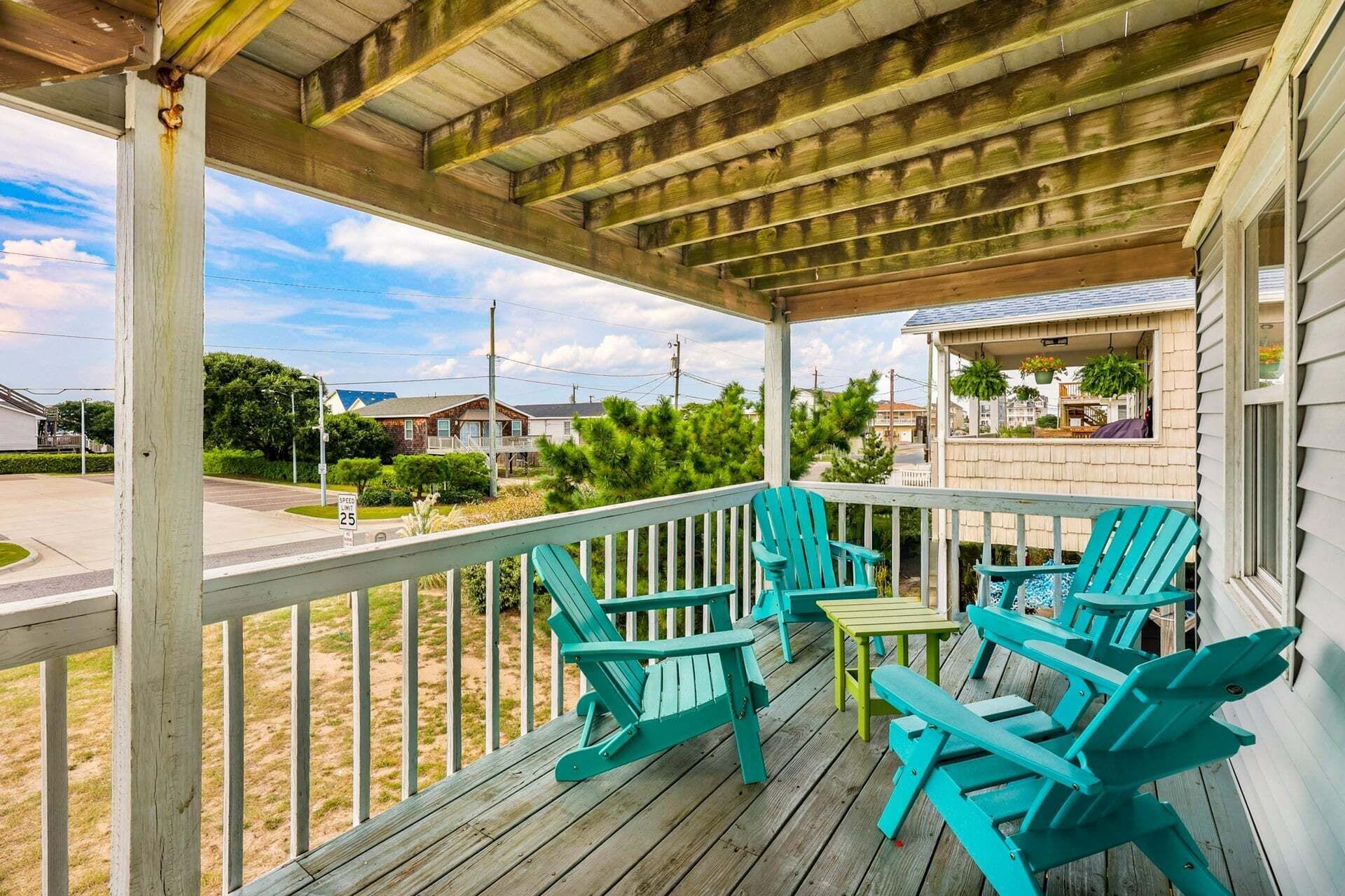 A covered porch with wooden railings and turquoise Adirondack chairs.