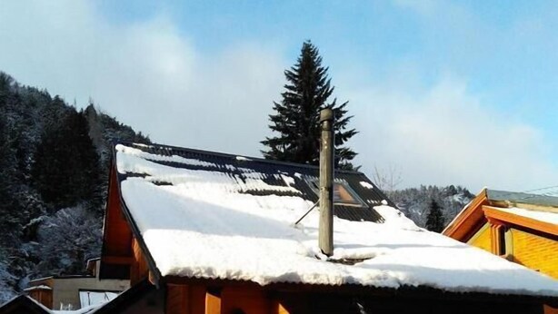 A wooden cabin with a snow-covered roof, a porch, and a visible chimney.