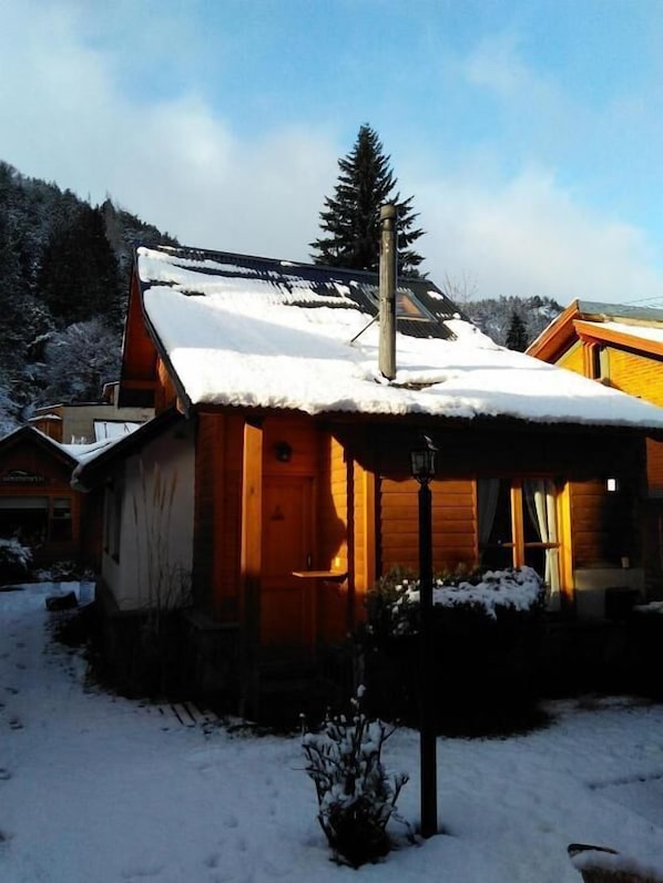 A wooden cabin with a snow-covered roof, a porch, and a visible chimney.