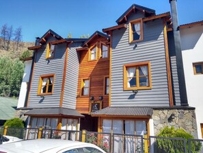 A multi-story building with a wooden facade, multiple windows, and a stone base. - Cabañas Aitue (San Martín de los Andes)