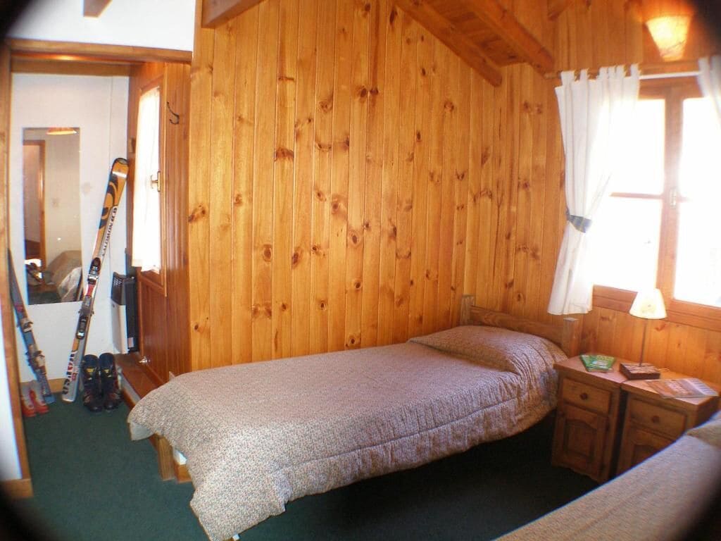 Una habitación de madera con una cama, una mesita de noche y un ventanal con cortinas.