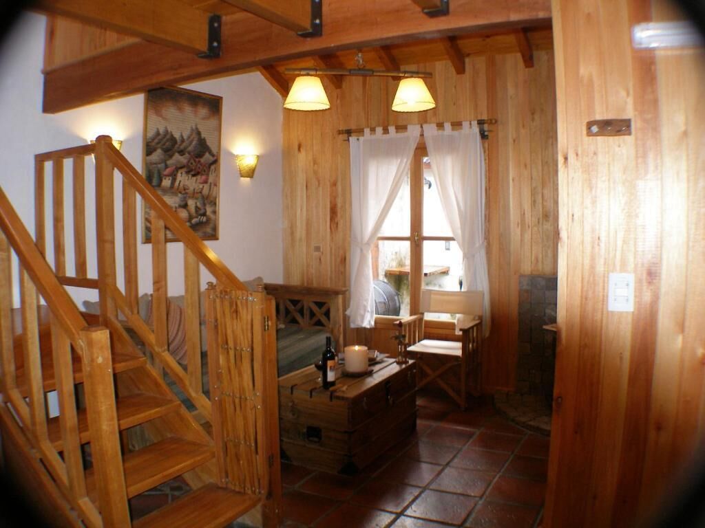 Interior de madeira com escada, uma mesa com uma garrafa e uma janela com cortinas.