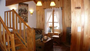 Interior de madeira com escada, uma mesa com uma garrafa e uma janela com cortinas.