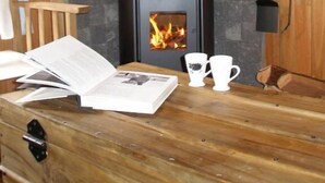 A room with a wood-burning stove, a wooden table with a book and two cups, and a stone fireplace.