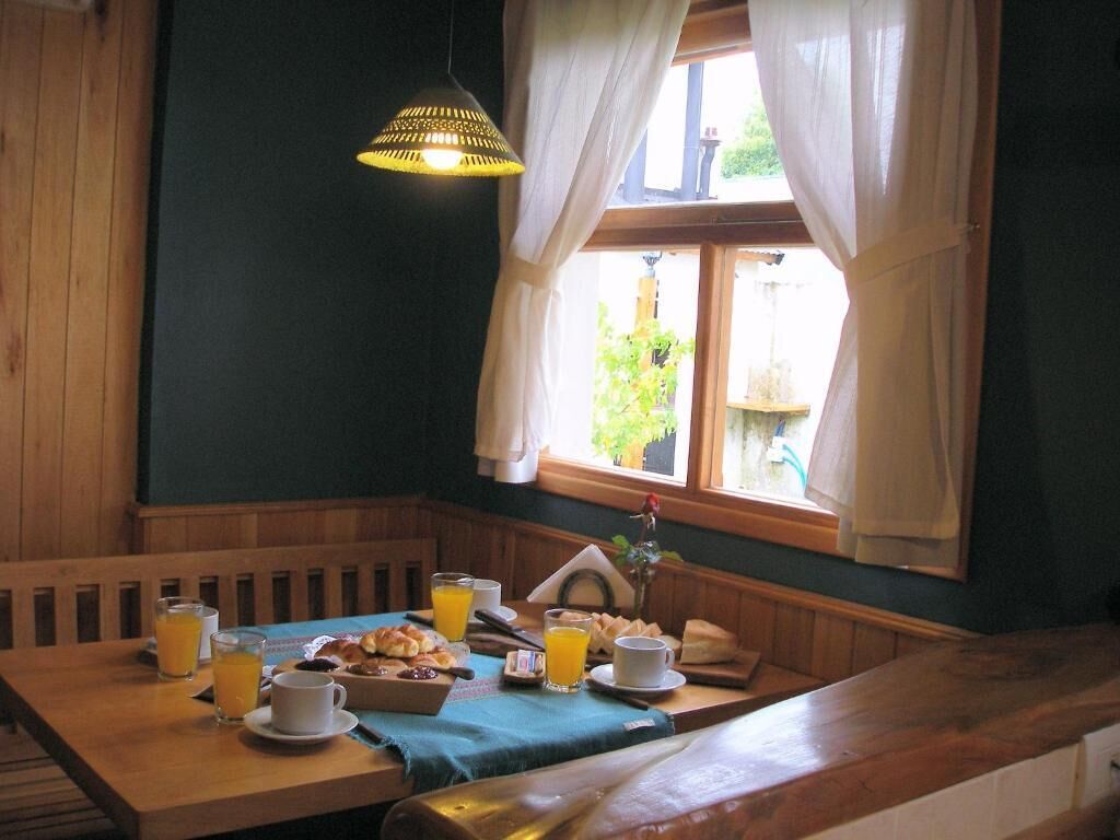 Una mesa de desayuno con jugo de naranja, una taza y pasteles en una habitación con paneles de madera y una ventana con cortinas.