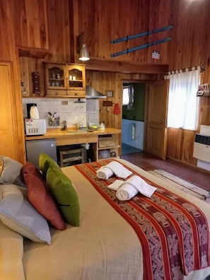 A room with a bed, a small kitchenette, and a door leading to another room.