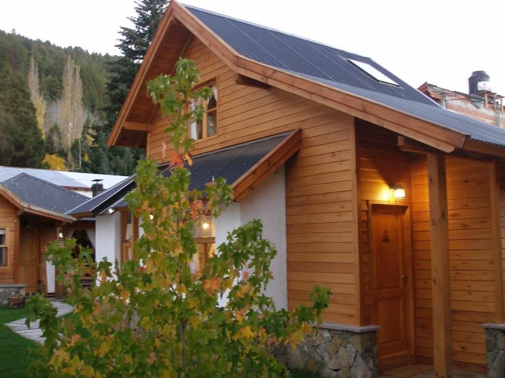 A wooden cabin with a sloped roof, a stone foundation, and a door with a light fixture.