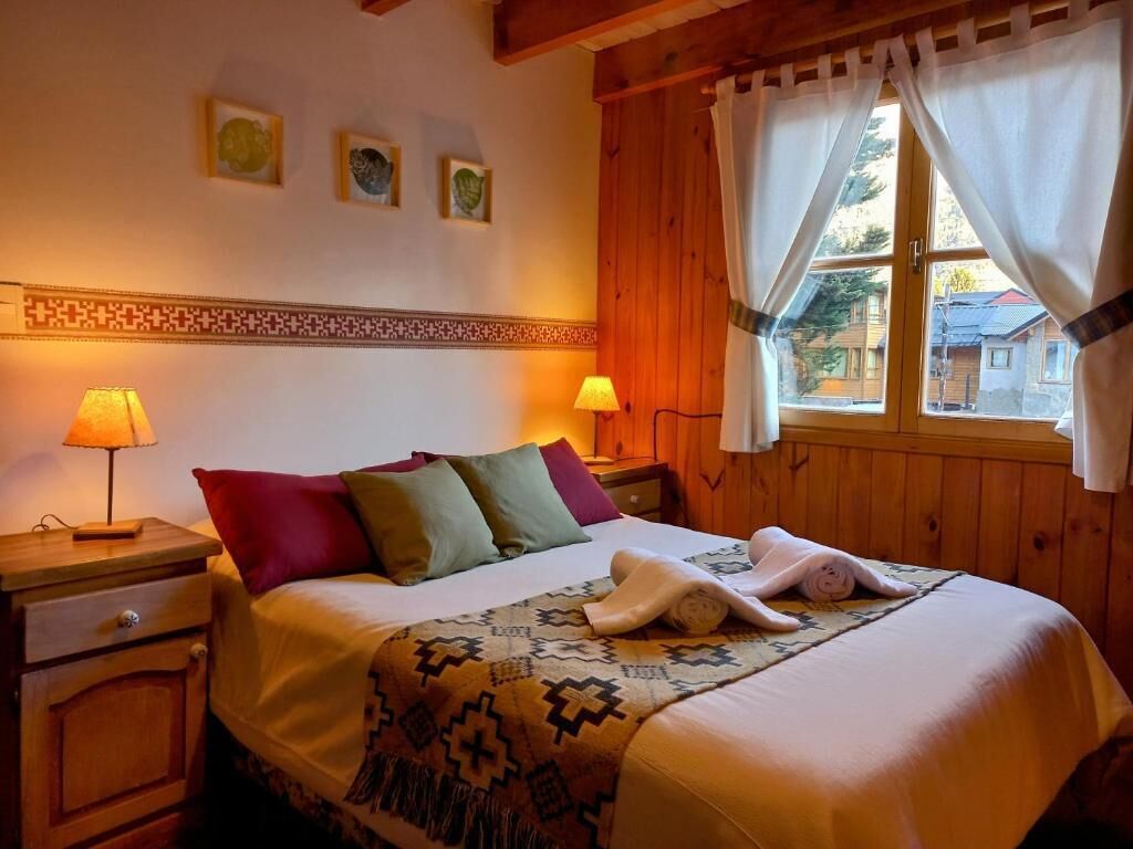 Um quarto acolhedor com uma cama, duas luminárias de cabeceira, uma janela com cortinas e uma parede com moldura decorativa.