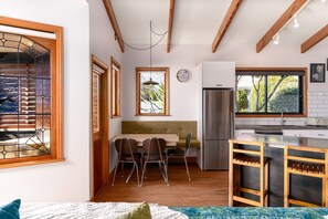 Une cuisine de taille réduite, équipée d’un réfrigérateur, d’un coin repas avec des chaises et d’une fenêtre donnant sur la verdure.