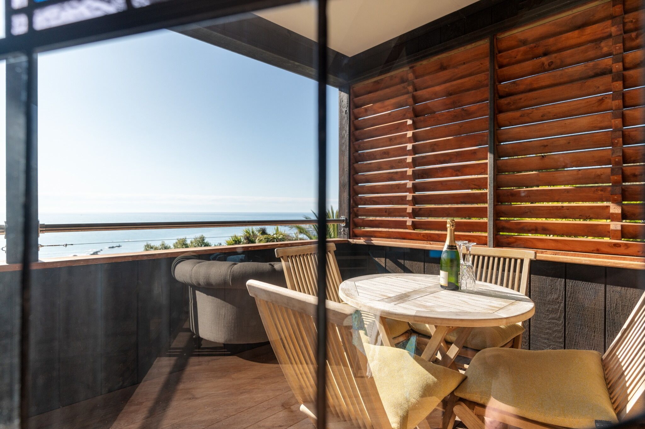 A balcony with a view of the sea, a round wooden table, and two cushioned chairs.