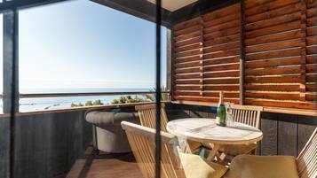 A balcony with a view of the sea, a round wooden table, and two cushioned chairs.