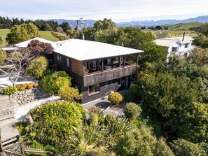 A two-story house with a balcony, surrounded by lush greenery and a mountainous backdrop. - Ocean Views Retreat | The Gallery Kaikōura (Kaikōura)