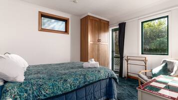 A bedroom with a bed, a wooden wardrobe, a window with a view, and a small table with a chair.