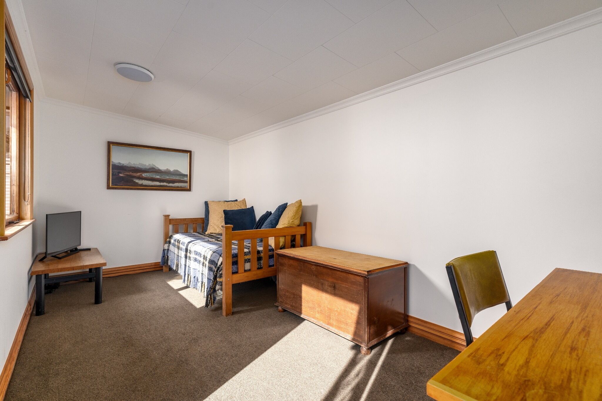 A room with a bed, a desk, a chair, a television, and a painting on the wall.