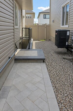 A residential outdoor area with a paved patio, a metal gate, and a gravel path.