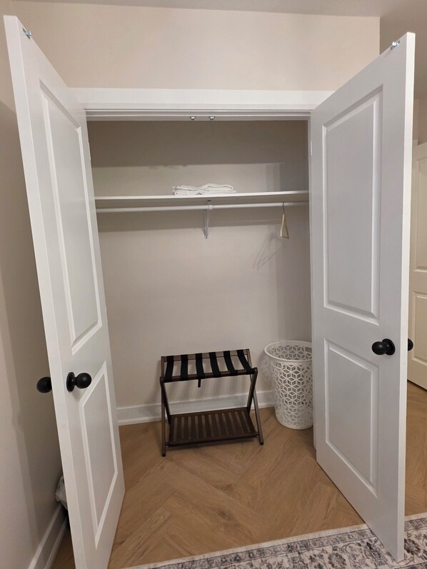 A closet with open doors, a small bench, and a laundry basket.