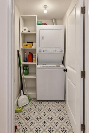 A laundry room with a washing machine, shelves with cleaning supplies, and a mop.