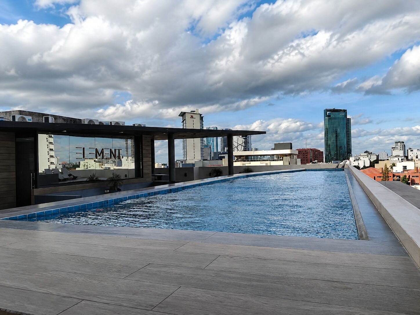 A rooftop swimming pool with a view of the city skyline, including modern buildings and a clear sky.