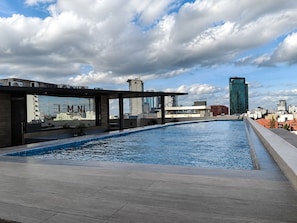 A rooftop swimming pool with a view of the city skyline, including modern buildings and a clear sky.