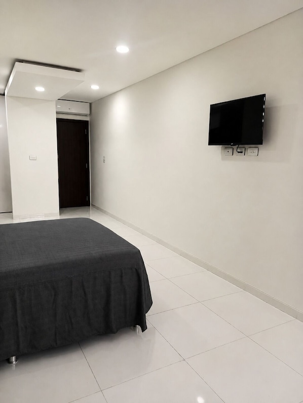 A hotel room with a bed, a television mounted on the wall, and a door leading to another room.