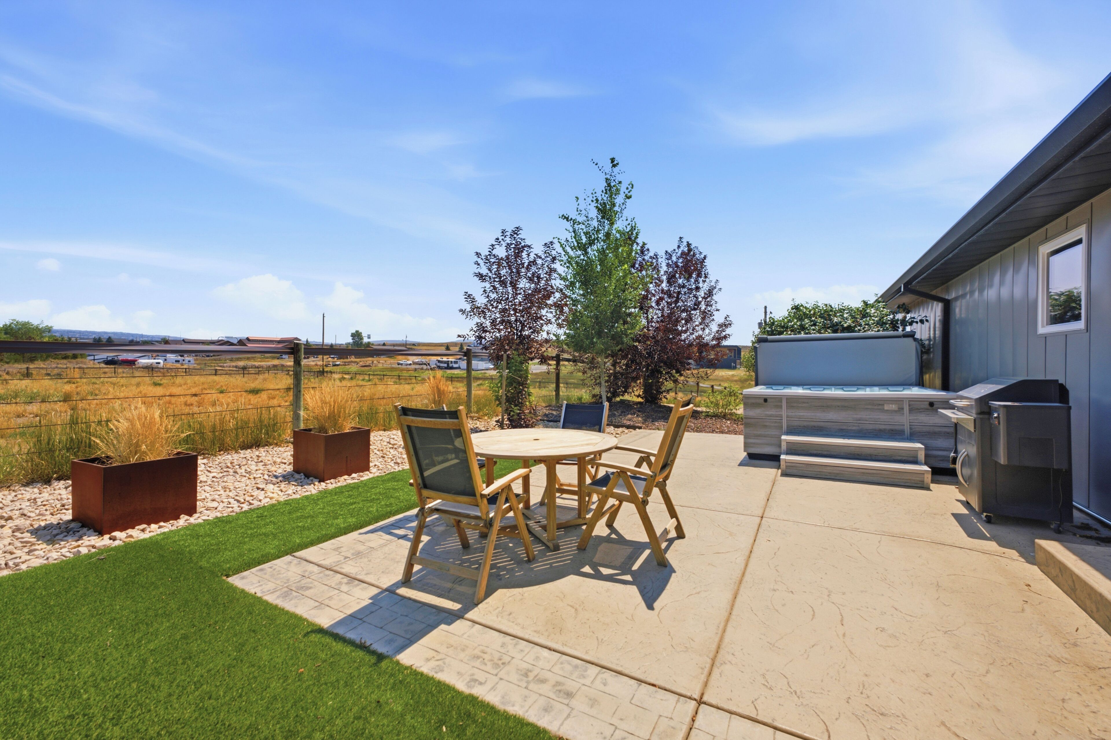 A patio with a table and chairs, a barbecue grill, and a view of a field.