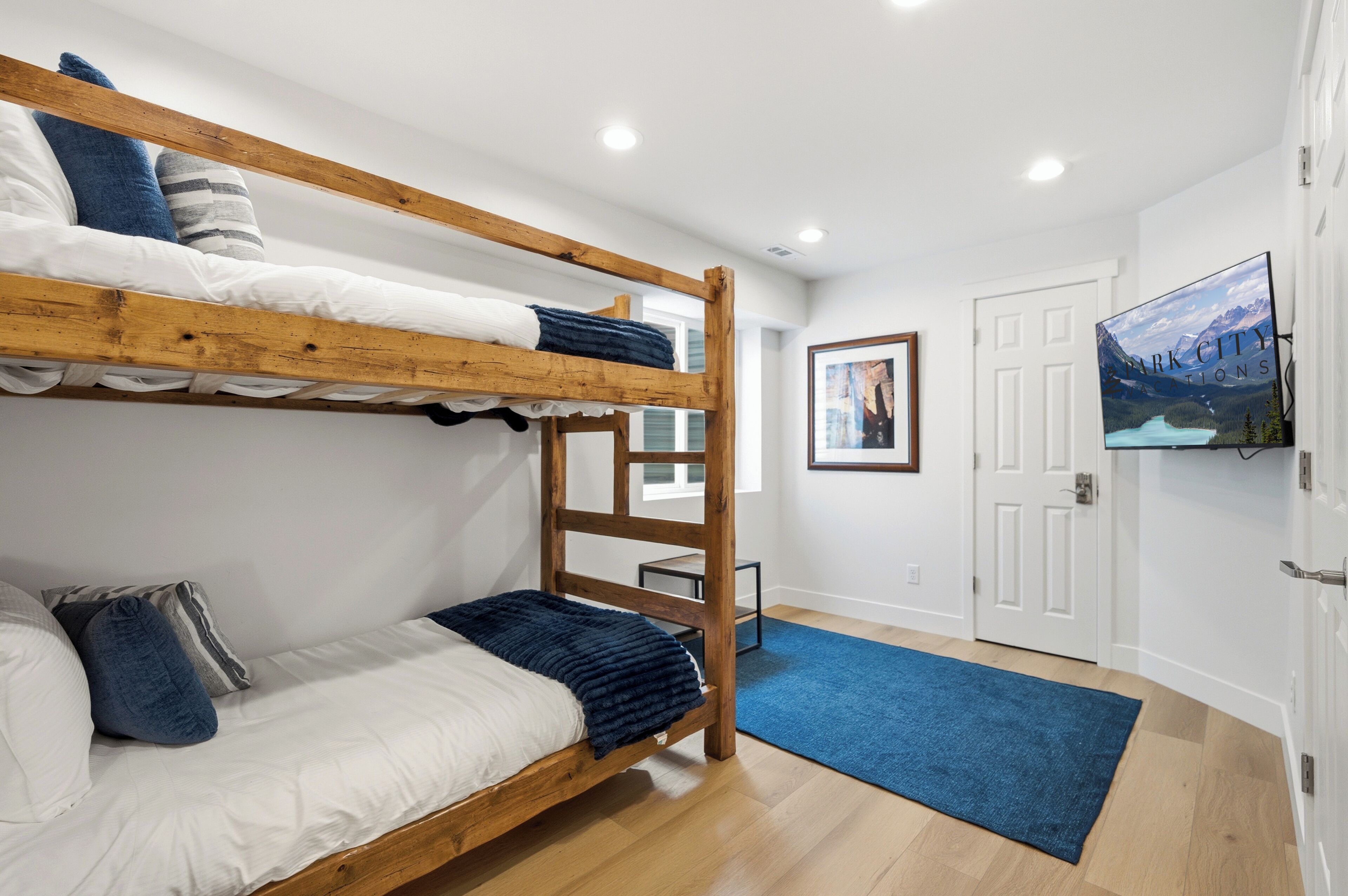 Une chambre avec un lit superposé en bois, un lit simple avec une literie blanche, une couverture bleue et un tapis bleu sur le sol.