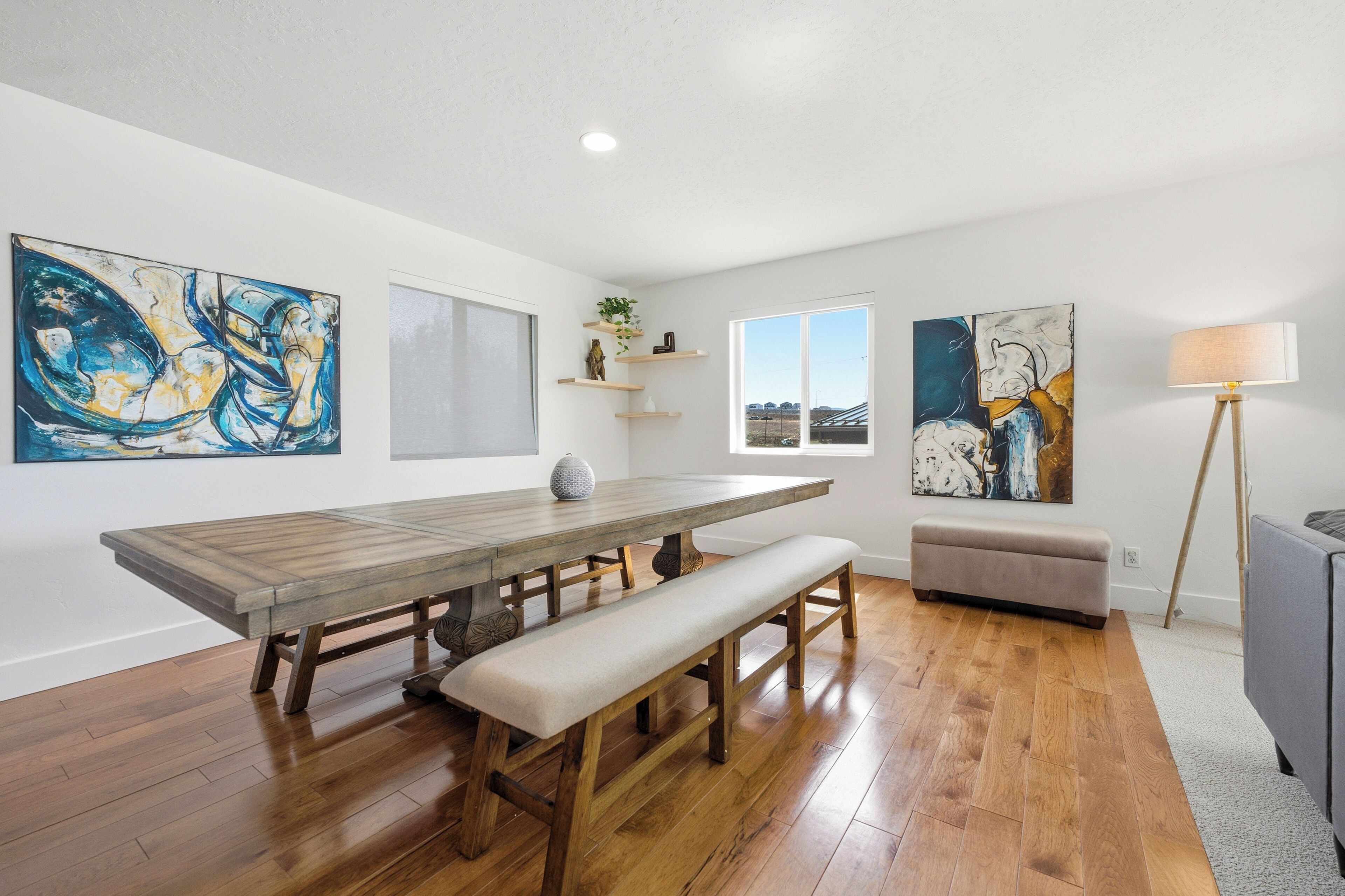 A dining area with a wooden table and benches, a window with a view, and abstract art on the walls.