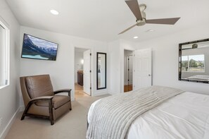 Ein Schlafzimmer mit einem Bett, einem Sessel, einem Deckenventilator, einem Gemälde und einer Tür zu einem anderen Raum.