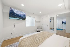 A bedroom with a bed, a TV mounted on the wall, a window with blinds, a chair, and a door leading to another room. - The Perfect Pace by Park City Vacations (Park City)