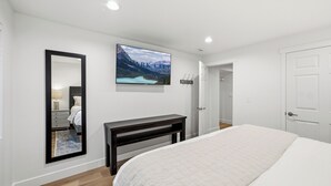 A bedroom with a bed, a bedside table, a mirror, a wall-mounted TV, and a door. - The Perfect Pace by Park City Vacations (Park City)