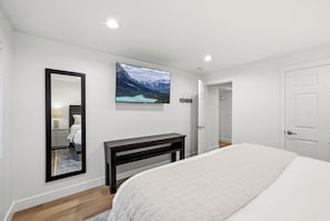 A bedroom with a bed, a bedside table, a mirror, a wall-mounted TV, and a door. - The Perfect Pace by Park City Vacations (Park City)