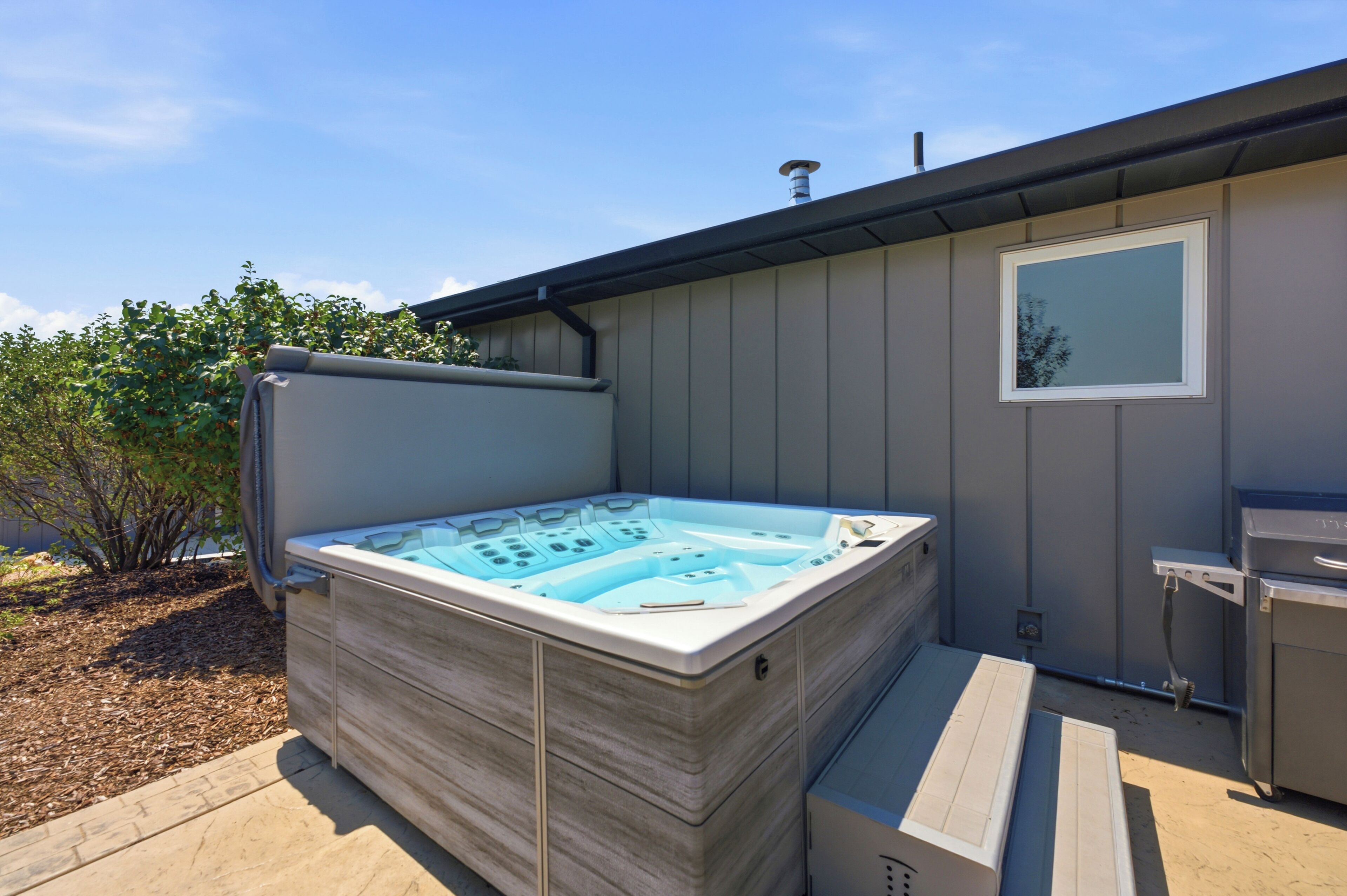 A hot tub with a control panel, a window, and a patio area with a wooden deck.
