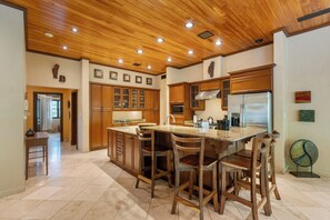A kitchen with wooden cabinets, a stainless steel refrigerator, and a central island with chairs. - 6 Bdr Penthouse with Plunge Pool and Beach Club Access! (Tamarindo)