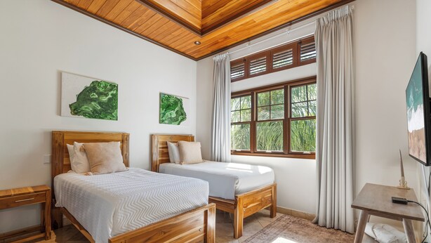 Un dormitorio con dos camas de madera, un ventanal con cortinas y una obra de arte en la pared.