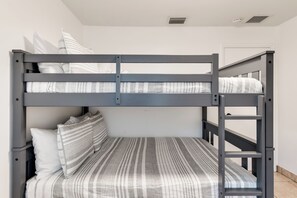 Ein Stockbett mit gestreifter Matratze und Kissen, eine Leiter sowie eine weiße Wand mit einer Tür im Hintergrund.
