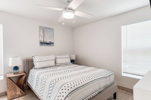 Ein Schlafzimmer mit einem Bett, einem Deckenventilator, einem Nachttisch, einer Lampe und einem Bild an der Wand.