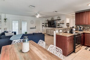 A modern kitchen with a central island, built-in appliances, and a dining area with a wooden table and white chairs. - Sunshine on Crestdale - 3/2 Pool home Sleeps 8 (Palm Beach Gardens)