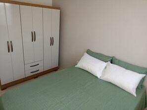 Ein Schlafzimmer mit einem Bett, grüner Bettwäsche und einem weißen Kleiderschrank mit Holzgriffen.