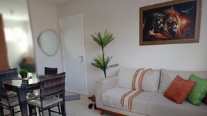 Una sala de estar con sofá, una mesa de comedor con sillas, una planta en maceta y un cuadro en la pared.