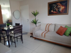 Ein Wohnzimmer mit einer Couch, einem Esstisch mit Stühlen, einer Zimmerpflanze und einem gerahmten Kunstwerk an der Wand.