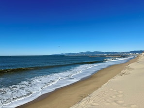 Ein Strand mit klarem Himmel, Wellen und einem fernen Steg.