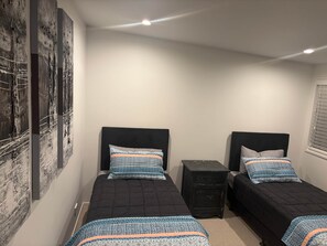 A bedroom with two beds, a small nightstand, and a wall-mounted artwork. - Sandy Soul Beach Apartment (Whitianga)