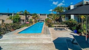 Eine Holzterrasse mit Pool, Liegestühlen und Kübelpflanzen.