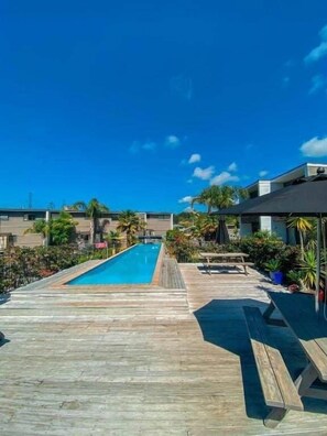 A wooden deck with a pool, lounge chairs, and potted plants. - Sandy Soul Beach Apartment (Whitianga)