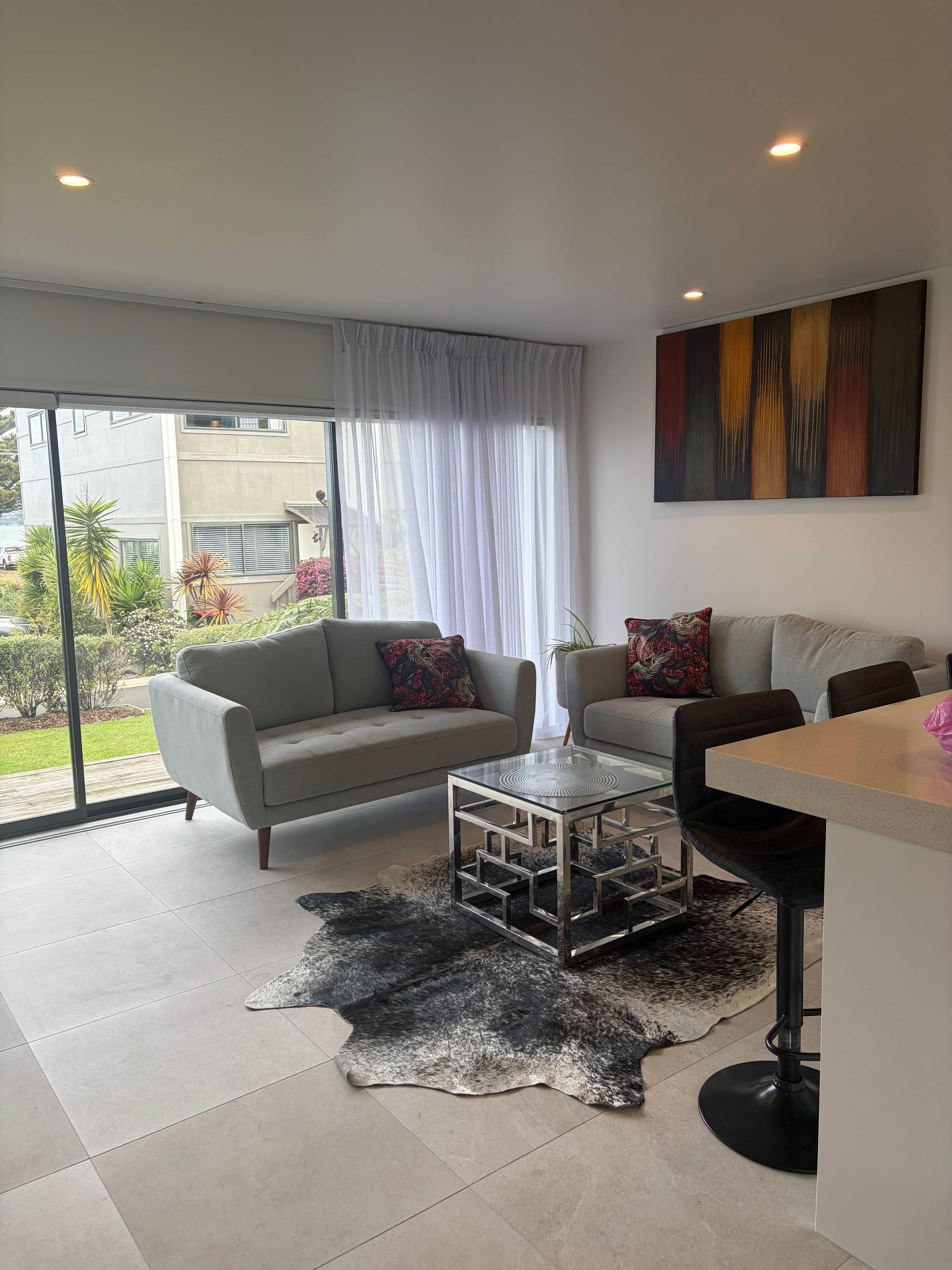 Una sala de estar moderna con un sofá, una mesa de centro de vidrio y un comedor con un taburete de bar.
