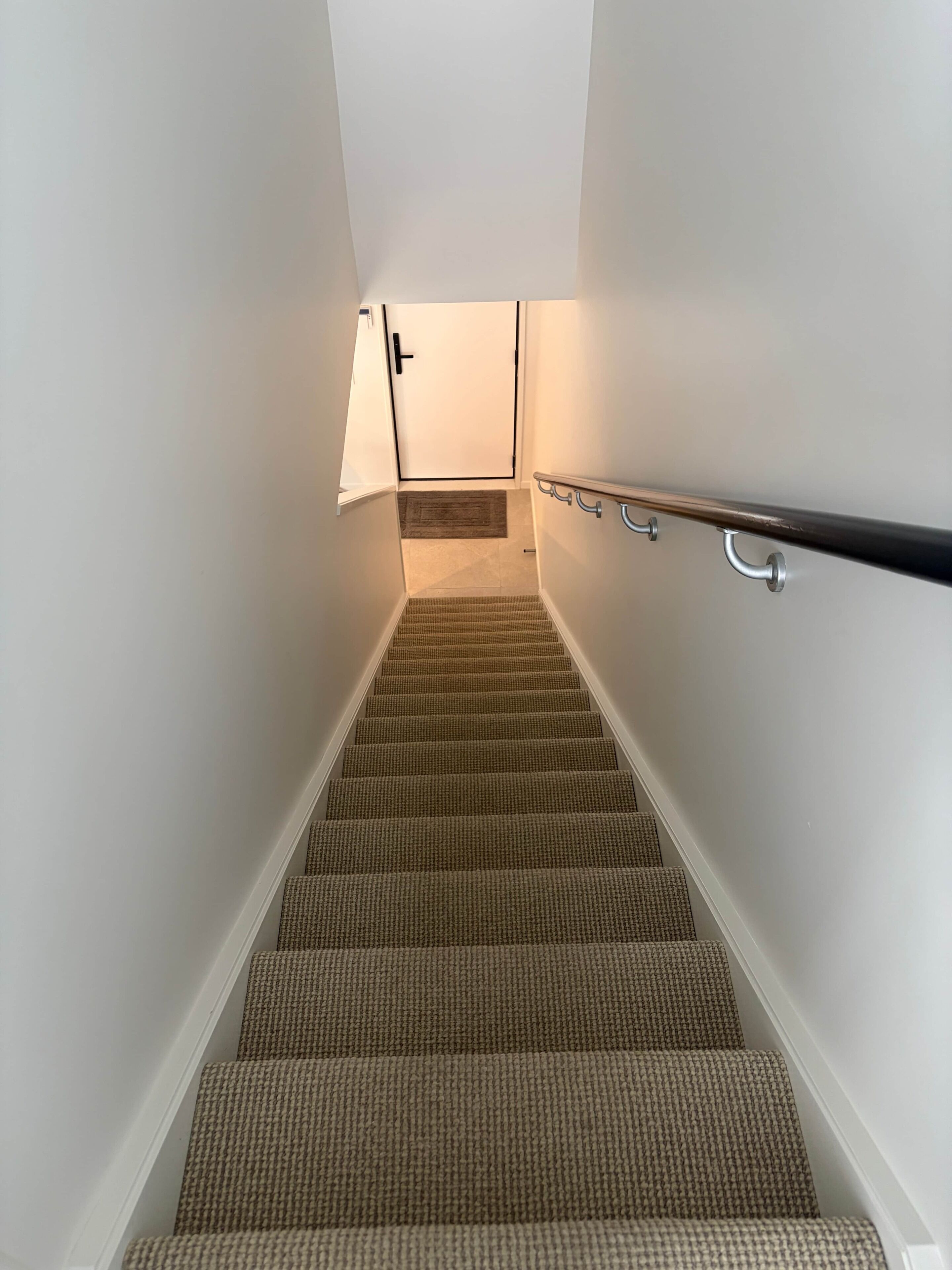 Un escalier recouvert de moquette, doté d’une rampe et d’une porte en haut.